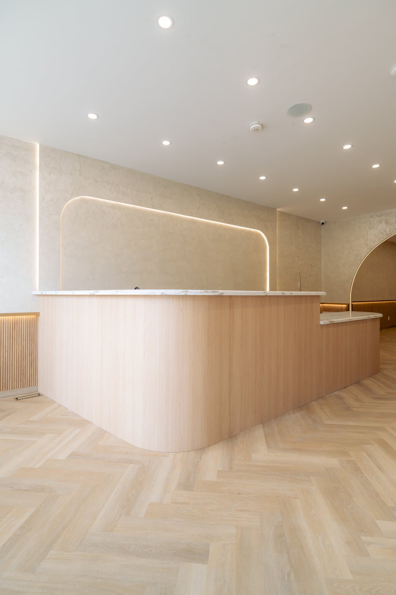Curved white oak service counter under a single marble slab