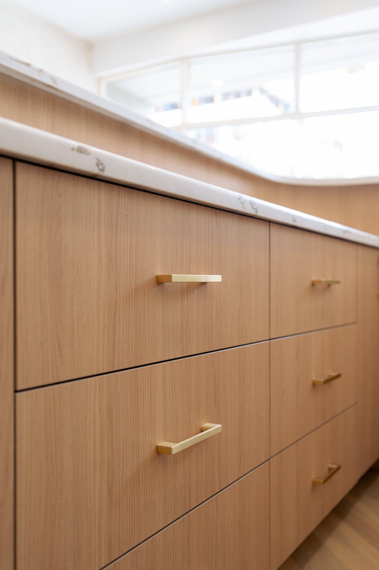 A bank of white oak drawers with slim brass pulls under a marble counter