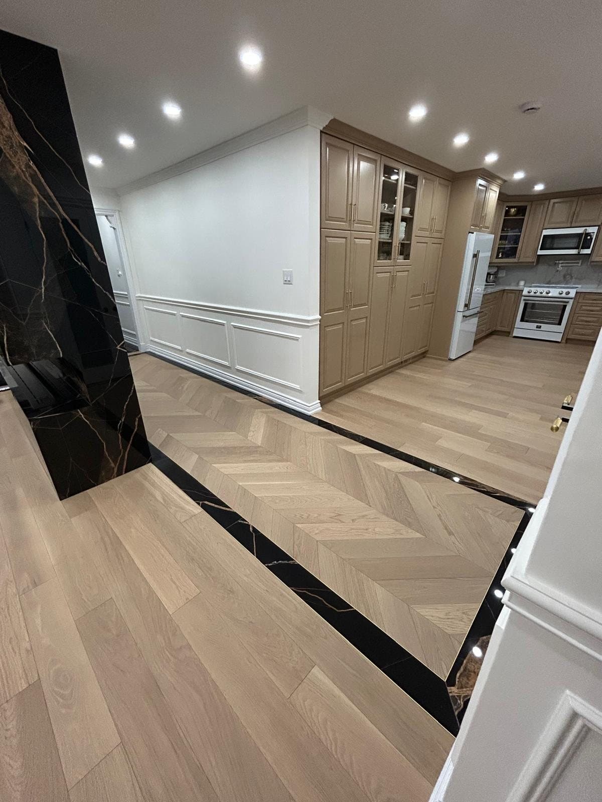 Chevron white oak floor running from a panelled hallway into a finished kitchen