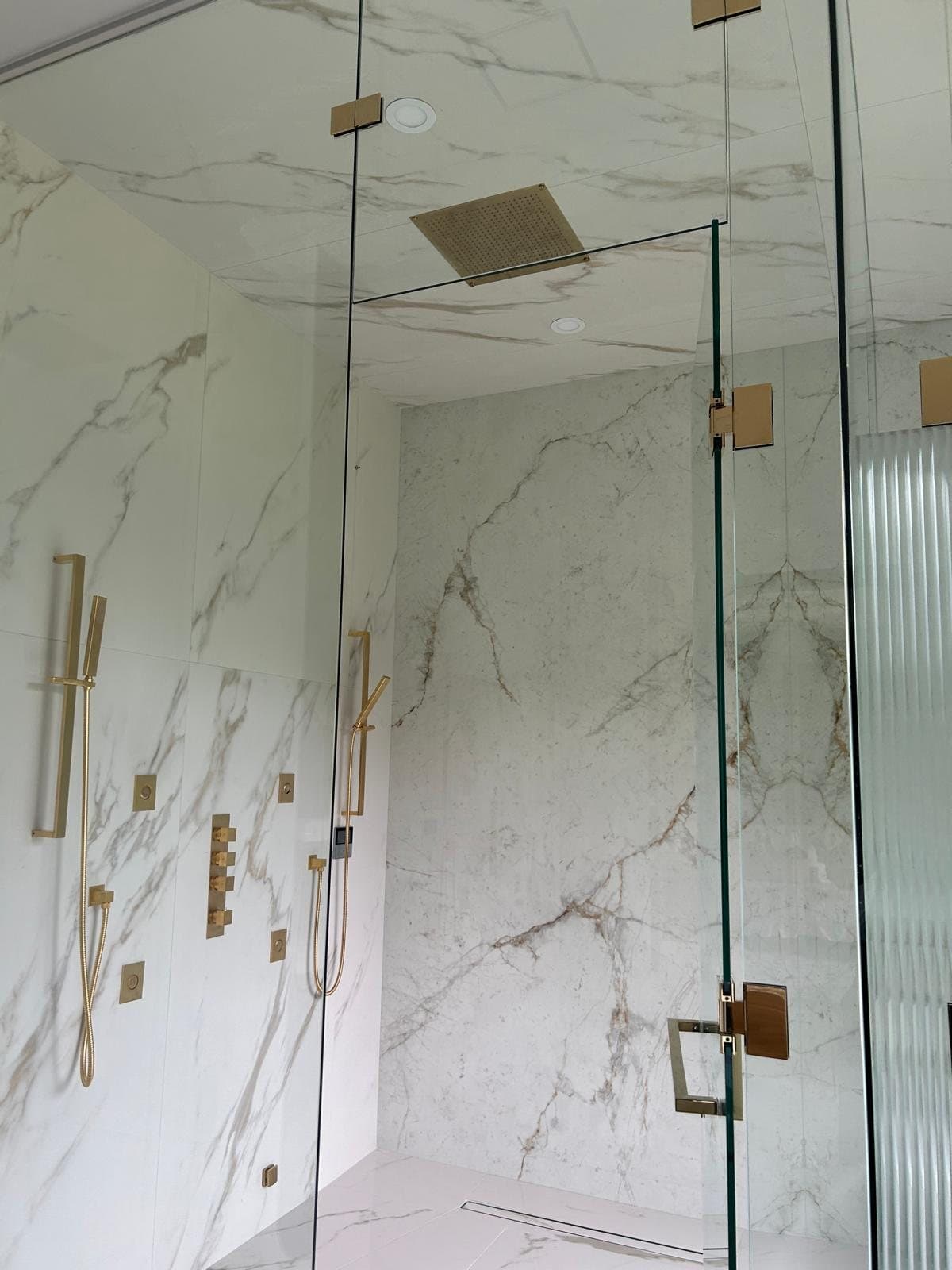 Calacatta slab shower with brass fixtures behind frameless glass