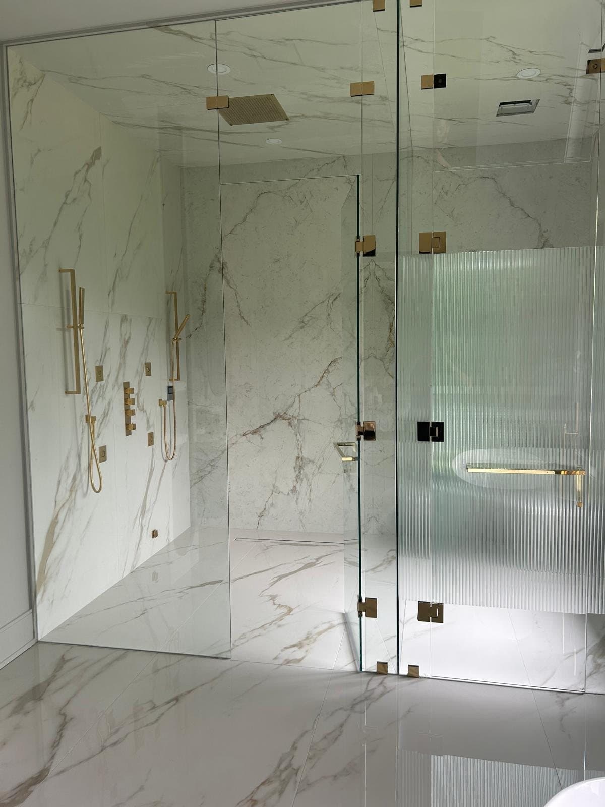 A Calacatta wet room with a frameless door and a reeded glass return panel